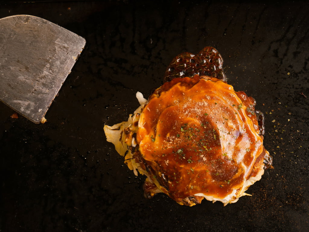 okonomiyaki, a deep-fried savory pancake dish. This was freshly cooked off the griddle, with a silver spatula on the side