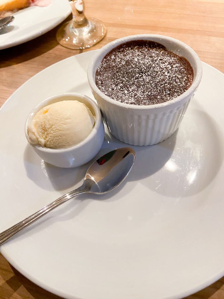 A ramekin of a chocolate cake that melts inside. It's powdered on top. Next to it is a small bowl of vanilla ice cream to eat with and a spoon. This chocolate melting cake was in the main dining room menu on the Carnival Radiance cruise, and is one of Carnival Cruise's most popular thing to eat..