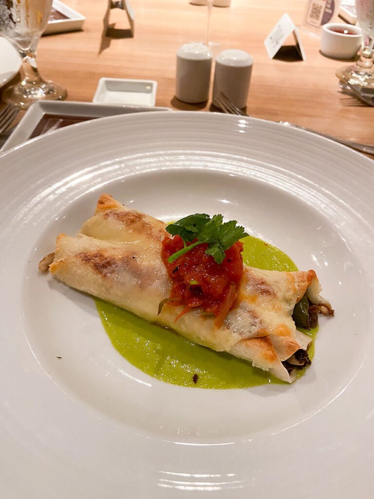 A plate of two enchiladas topped with salsa and a sprig of parsley, in the main dining hall on Carnival Radiance cruise as a part of one of the dinner options