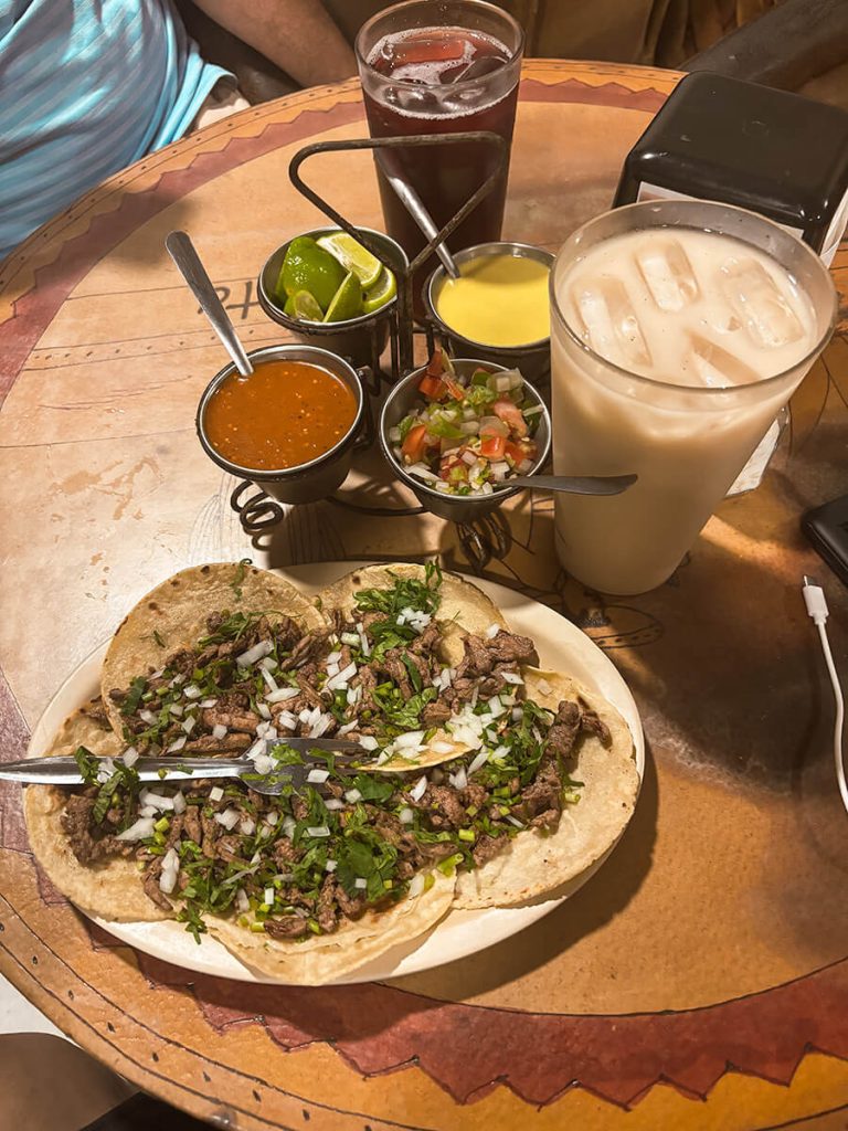 A table of 5 tacos served with 3 types of salsa, lime, and a cup of horchata and jamaica. This is in Taquitos Acapulco Vallarta, a sit-down taco restaurant in Puerto Vallarta, Mexico