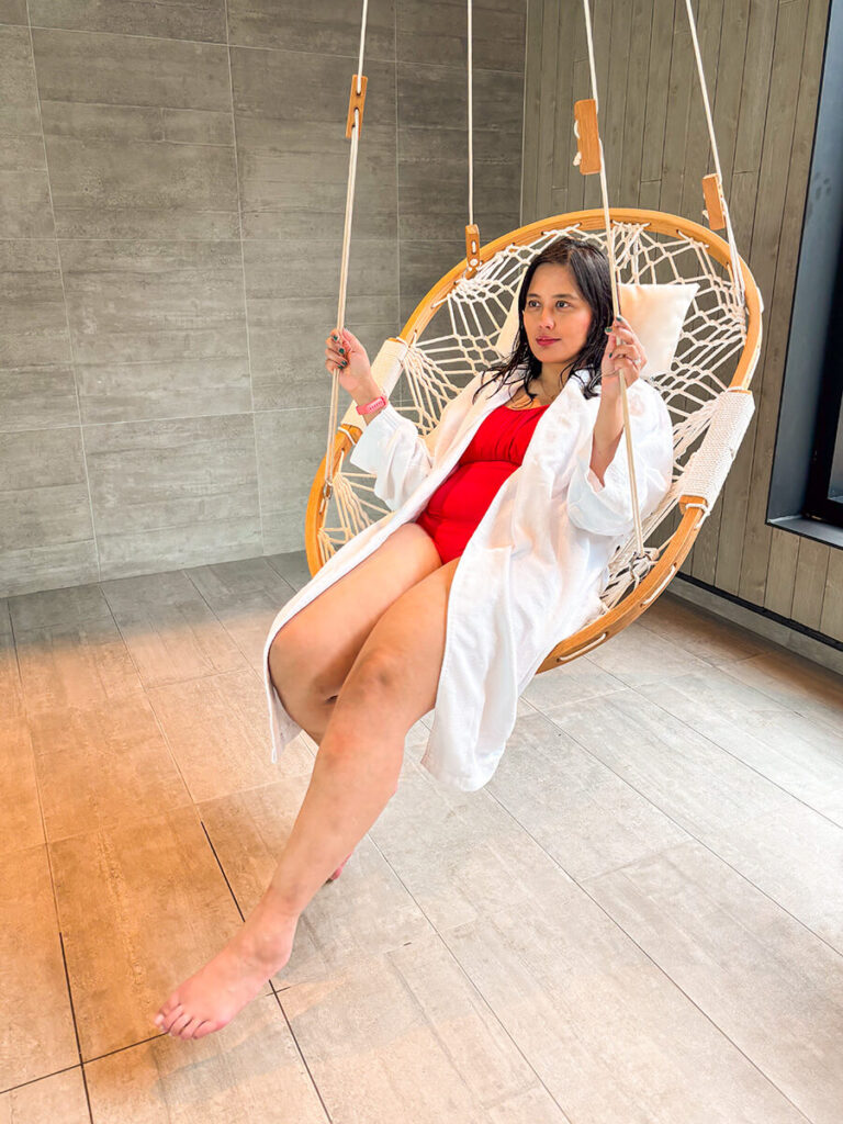 Hannah sitting on a hanging chair in Strom Spa in Quebec City, wearing a white robe and a red one piece bathing suit under