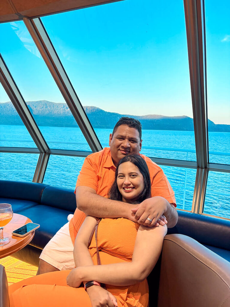 Hannah and Cecilio sitting in Crow's Nest Bar on Holland America Zaandam, dressed in orange outfits for the Orange Party