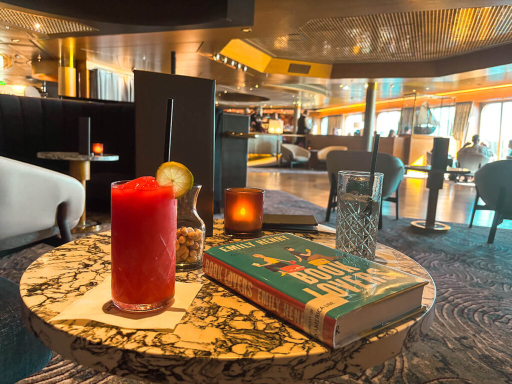 A table in Ocean Bar on Holland America Zaandam. On top of the table, there's a strawberry daquiri, a glass jar of peanuts, a candle, and a glass of water