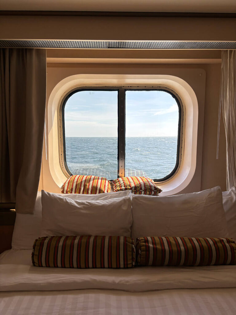 Ocean view room from Holland America Zaandam, with the bed wedged against the window and view of the ocean from the Inside Passage in Alaska