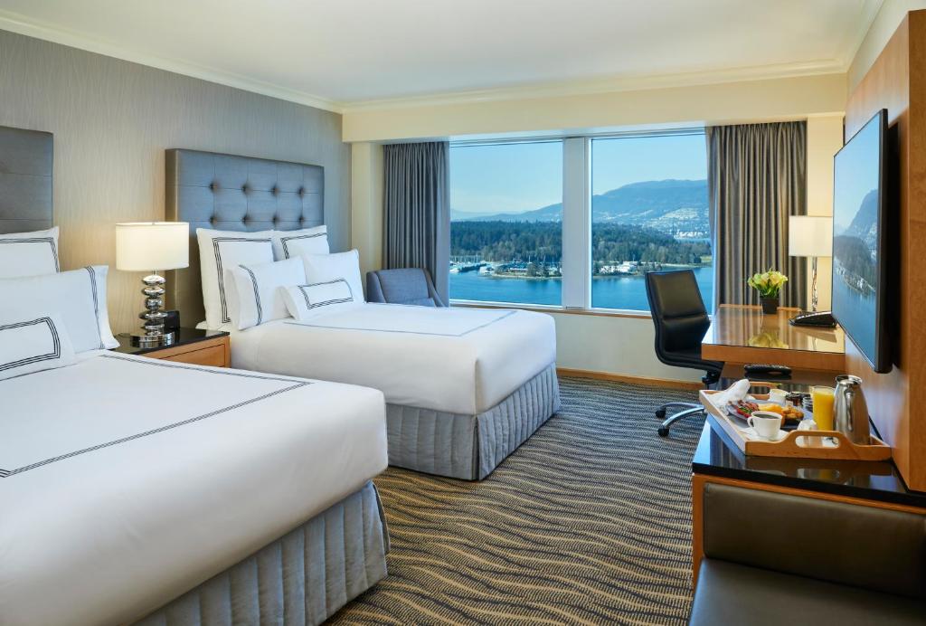 Two queen beds in Pan Pacific Vancouver overlooking the water and North Shore Mountains, with a desk and a tray of breakfast