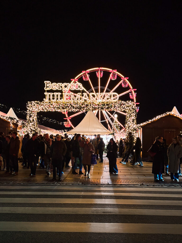 The Christmas market in Bergen, Norway at night. This is the entrance, with lights and the sign that says "Bergen Julemarked". There is a ferris wheel behind
