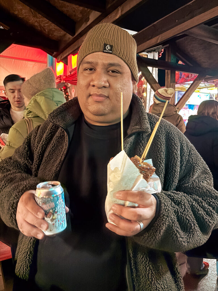 Cecilio at Bergen Christmas market holding a Christmas soda and moo ping, Thi pork skewers