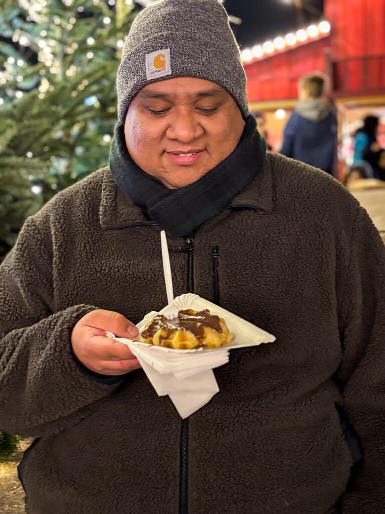 Cecilio smiling and looking at his Belgian waffles with powder and chocolate sauce at the Højbro Plads Christmas market in Copenhagen
