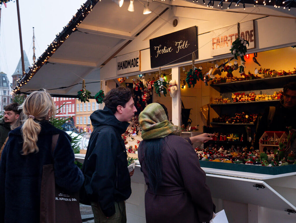 A woman and a man pointing at some of the gifts at a cabin at the Nyhavn Christmas market in Copenhagen.