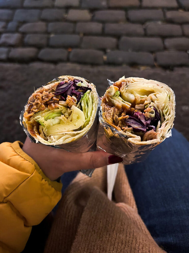 Hannah holding a wrap with raclette cheese, cabbage and pulled pork at the Højbro Plads Christmas market in Copenhagen