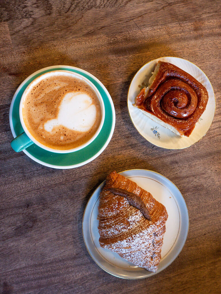 A flat lay of a latte, orange cinnamon roll, and nutella croissant from BUKA Bakery in Copenhagen