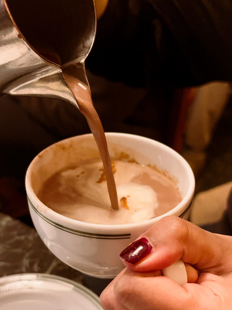 Hannah holding a cup of hot chocolate form Conditori La Glace in Copenhagen on one hand, and pouring it from the pot on the other